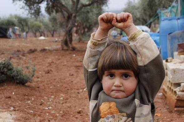 Bé Adi Hudea, 4 tuổi, người Syria mím chặt môi và giơ tay đầu hàng vì tưởng máy ảnh là súng khi phóng viên chụp em tại trại tị nạn Atmen ở biên giới Syria - Thổ Nhĩ Kỳ. Ảnh: Daily Mail