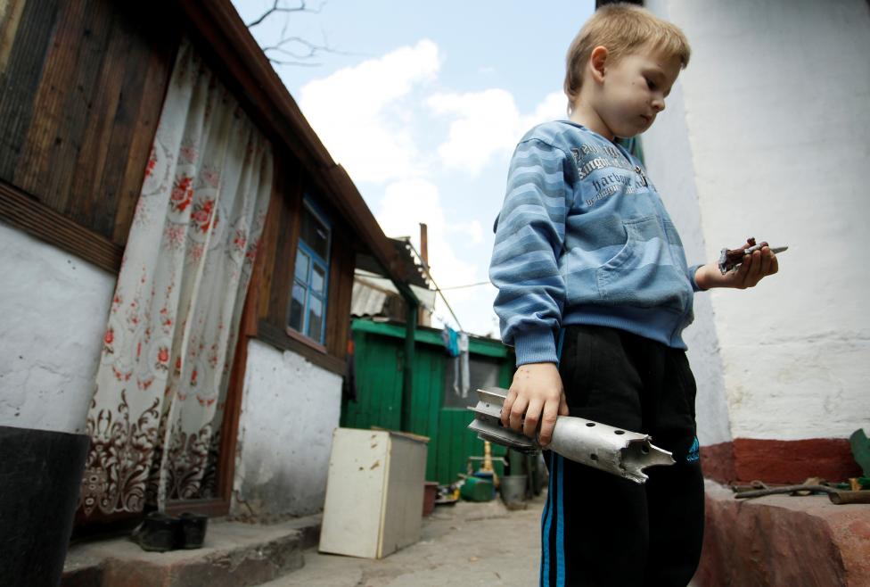 Một cậu bé đang cầm trên tay mảnh vỏ đạn cối sau vụ tấn công vào ngôi làng ở Staromykhailivka, bên ngoài khu vực biệt lập Donetsk, Ukraina