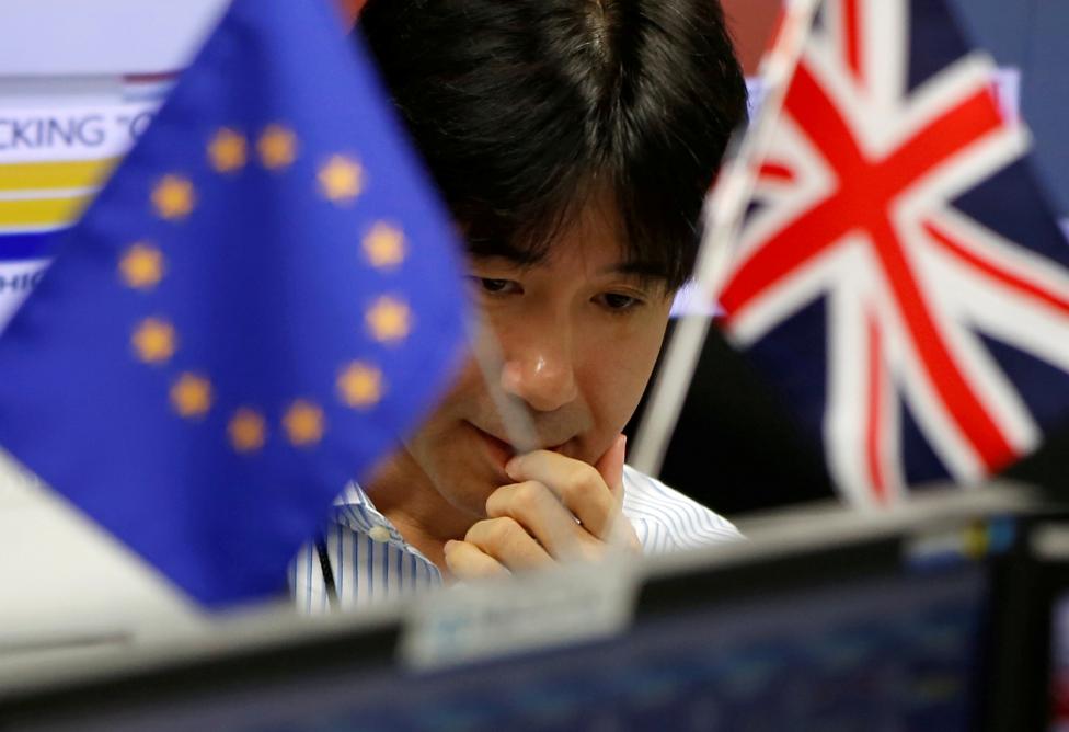 Một nhân viên công ty thương mại giao dịch quốc tế ở Tokyo đang làm việc. Phía trước mặt anh là hai lá cờ của Anh và EU.