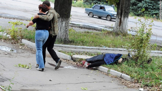 Người dân địa phương đi ngang qua xác chết của một nạn nhân mất mạng trong vụ đánh bom – một chuyện dường như đã quá quen thuộc ở thành phố Donetsk