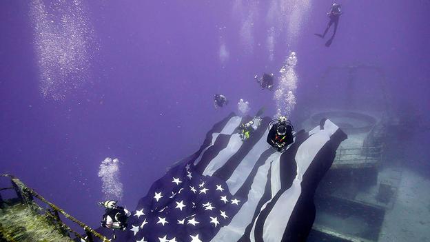 Thợ lặn giăng một lá cờ lớn trên tàu Hải quân Hoa Kỳ Hoyt S Vandenberg đã bị chìm trước để tạo thành một rạn san hô nhân tạo trên bờ biển Florida cách đây năm năm. (tin tức Văn phòng Florida Keys / Reuters).