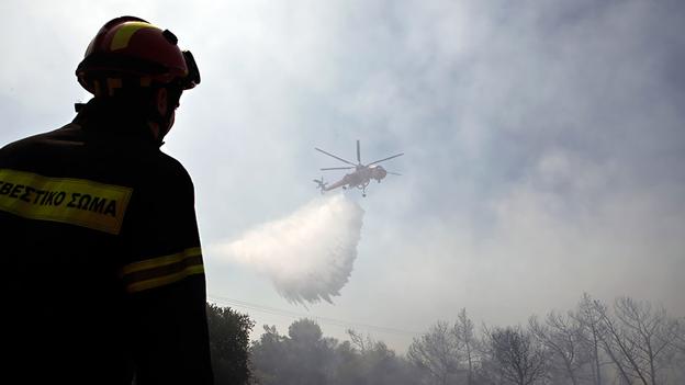 Trực thăng ném bom nước. Một lính cứu hỏa quan sát chiếc máy bay trực thăng đang dội nước dập tắt một đám cháy gần thủ đô Athens của Hy Lạp. (Reuters)