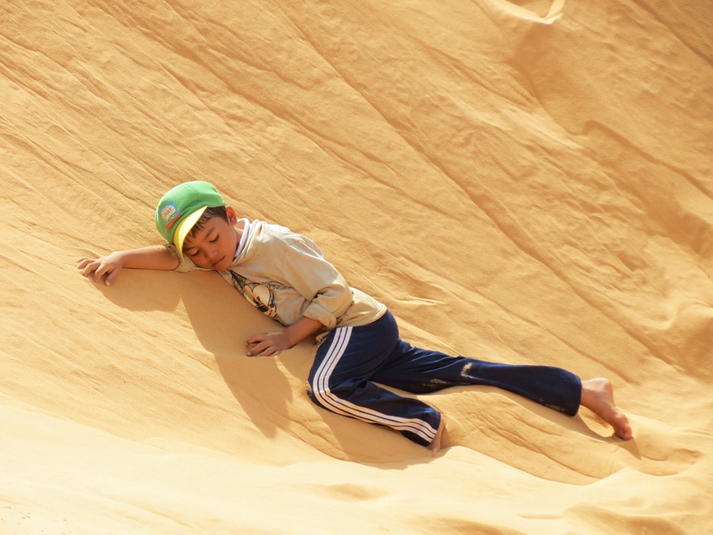 Phút giây nghỉ ngơi của bé trai ở Mũi Né (Bình Thuận) vào tầm trưa. Em cùng gia đình kiếm sống bằng việc cho du khách thuê miếng trượt cát hàng ngày. Ảnh: Zing News