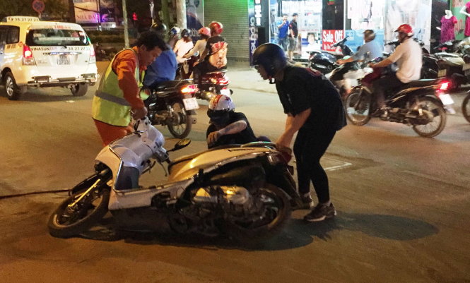 Nhân viên dọn dẹp cát dựng xe giúp hai người đi xe máy té ngã tại hiện trường vụ tai nạn giao thông