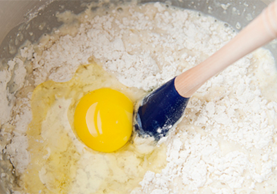 Cho tất cả các nguyên liệu khô vào tô lớn, sau đó đổ từ từ hỗn hợp sữa trên và 1 quả trứng vào. Sau đó, trộn đều tay, vừa trộn vừa thêm bột vào cho đến khi bột săn lại và không còn bị dính vào thành tô nữa là được. Sau đó, chuẩn bị 1 tô khác, phết bơ vào tô rồi cho bột vào ủ trong khoảng 1 giờ.