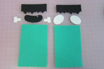 Cắt 2 tấm vải dạ xanh hình chữ nhật làm khuôn mặt, 2 tấm vải đen làm tóc và miệng, 2 tấm vải trắng hình oval làm đôi mắt và đôi tai.