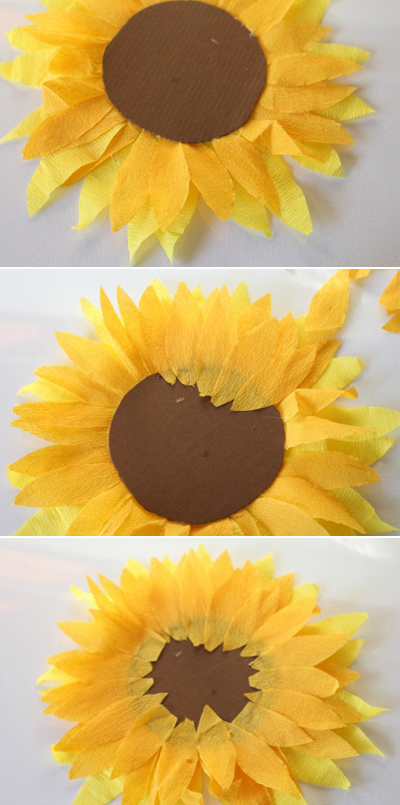 Lật mặt sau của tấm giấy hình tròn vừa dán các cánh hoa lên rồi dán lớp cánh hoa thứ ba màu cam xung quanh hình tròn, sao cho các cánh hoa xen kẽ với lớp cánh hoa cam thứ nhất bên dưới hình tròn.