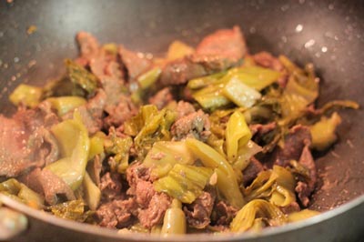 Khi thịt tái thì bỏ dưa chua vào, thêm chút hạt nêm và đảo đều để cho dưa ngấm gia vị và dầu ăn. Đổ thịt bò xào dưa ra đĩa.