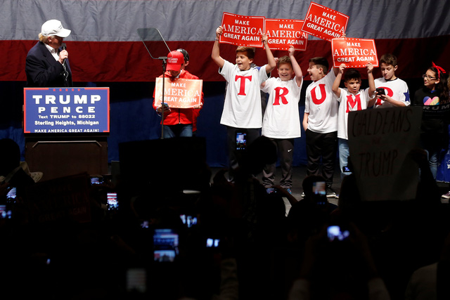 Ông Trump xuất hiện trên sân khấu tại cuộc vận động tranh cử ở Detroit, bang Michigan hôm 6/11. Đứng kế bên ông là các học sinh mang theo khẩu hiệu tranh cử “Làm cho nước Mỹ vĩ đại trở lại” của ứng viên đảng Cộng hòa.