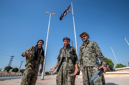 Những tay súng thuộc Các đơn vị Bảo vệ Nhân dân người Kurd đứng cạnh cờ Nhà nước Hồi giáo ở thị trấn Tel Abyad, Syria