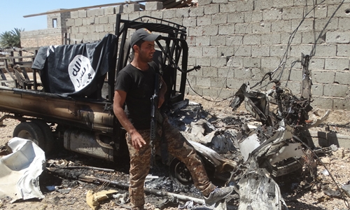 Lính Iraq đứng cạnh một chiếc xe của nhóm khủng bố IS đã bị phá hủy trong cuộc tấn công nhằm giành lại thị trấn Heet