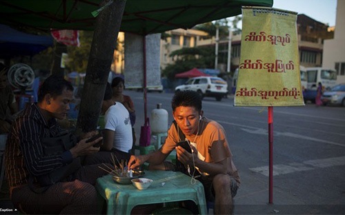 Người đàn ông Myanmar sử dụng điện thoại di động khi đang ngồi quán vỉa hè ở Yangon, Myanmar. Ảnh: Bloomberg.