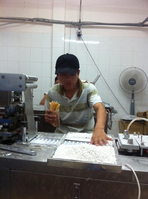 Công nhân vừa ăn vừa dùng tay trần đưa thực phẩm chức năng viên vào máy dập vỉ.
