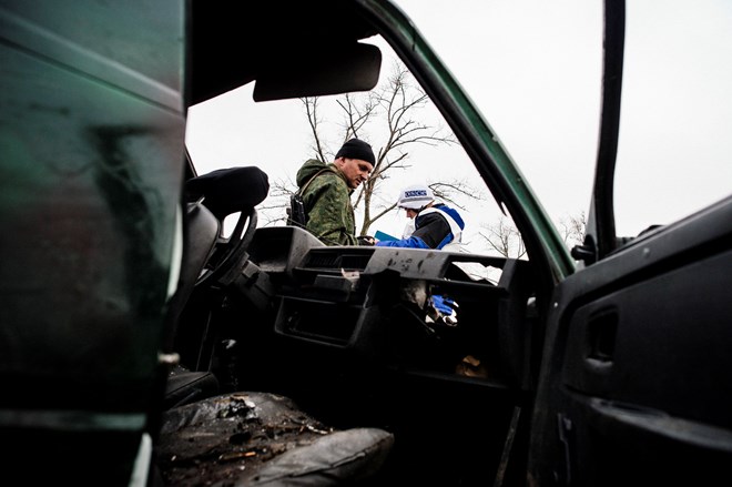 Một lính phe ly khai và một quan sát viên quốc tê của tổ chức OSCE đứng bên cạnh một chiếc xe bị phá hủy